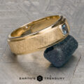 A "Stacked from 49 images. Method=B (R=7,S=2)" ring in 14K yellow gold, featuring a striking blue gemstone, rests on a rough dark mineral sample atop a textured gray surface. The words "Earth's Treasury" appear at the bottom.