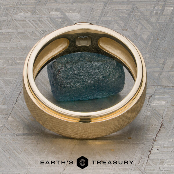 Stacked from 48 images. Method=B (R=7,S=2) A Stacked from 48 images. Method=B (R=7,S=2) ring crafted in 14K Yellow Gold, featuring a blue rough gemstone at its center, is displayed on a textured metallic surface with a delicate Florentine Finish. The logo and text "Earth's Treasury" appear at the bottom.