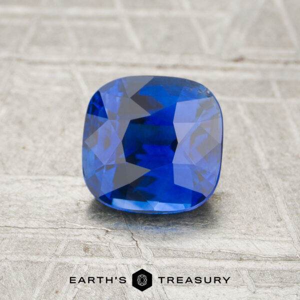 1.21-Carat Sapphire A 1.21-carat cushion-cut blue sapphire rests on a textured surface above the “Earth’s Treasury” logo.