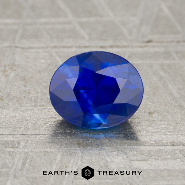 1.18-Carat Sapphire A 1.18-carat oval-cut blue sapphire displayed on a textured surface, with "EARTH’S TREASURY" and a hexagonal logo beneath.