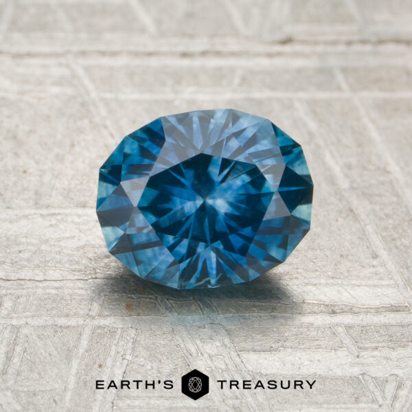 1.35-Carat Teal Blue Montana Sapphire (Heated) A 1.35-carat heated Montana sapphire is displayed on a light textured surface with the EARTH'S TREASURY logo and text below it.