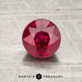 A 1.21-carat round, faceted ruby is displayed on a textured, light background with "EARTH'S TREASURY" written below.