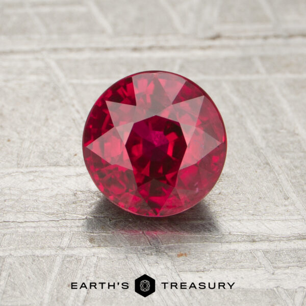 A 1.21-carat round, faceted ruby is displayed on a textured, light background with "EARTH'S TREASURY" written below.
