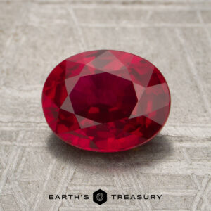 A 2.20-carat ruby, faceted in an oval shape, rests on a textured metallic surface with the Earth's Treasury logo and text below.