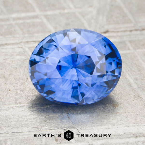 1.72-Carat Sapphire A 1.72-carat faceted blue sapphire is shown on a textured gray surface with "EARTH'S TREASURY" displayed at the bottom.