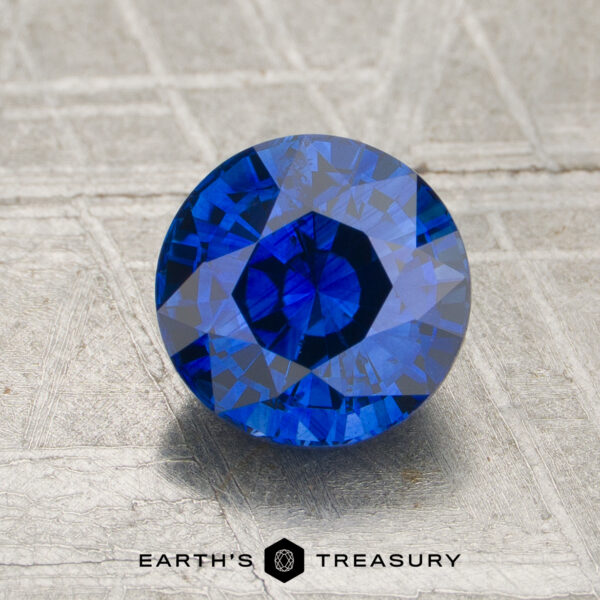 1.62-Carat Sapphire A 1.62-carat round-cut blue sapphire is displayed on a textured surface with the "Earth's Treasury" logo at the bottom.