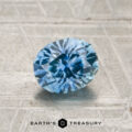 A 1.17-carat heated Montana sapphire is displayed on a textured, light-colored surface, with the Earth's Treasury logo and text at the bottom.