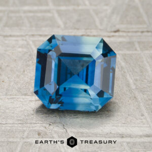 A 1.30-carat sapphire with a square step cut is displayed on a textured gray surface, with "Earth's Treasury" written at the bottom.