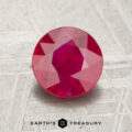 A 1.30-carat round, faceted ruby is displayed on a gray textured surface with the words "EARTH'S TREASURY" below it.