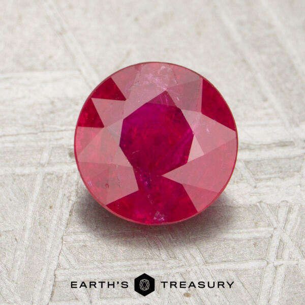 1.30-Carat Ruby A 1.30-carat round, faceted ruby is displayed on a gray textured surface with the words "EARTH'S TREASURY" below it.