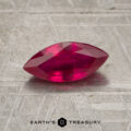 A 0.96-carat marquise-cut ruby is displayed on a textured metallic surface with the text "EARTH'S TREASURY" at the bottom.