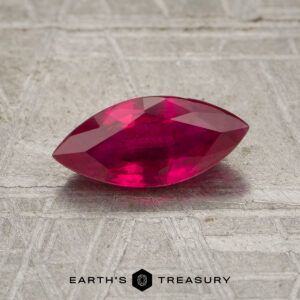 A 0.96-carat marquise-cut ruby is displayed on a textured metallic surface with the text "EARTH'S TREASURY" at the bottom.