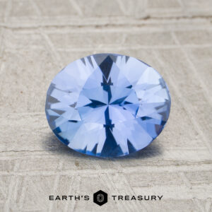 A 1.53-carat unheated Ceylon sapphire with an oval faceted cut is displayed on a light textured surface, with "Earth's Treasury" shown below.