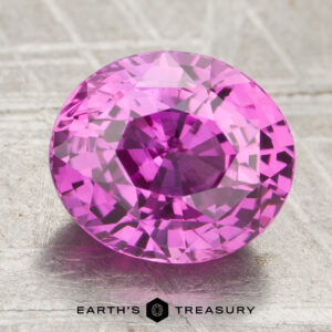 A 3.07-carat heated oval pink sapphire displayed on a textured gray surface, featuring the Earth's Treasury logo at the bottom.