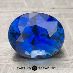 A 3.05-carat heated sapphire gemstone is displayed on a textured surface with the words "Earth's Treasury" beneath it.