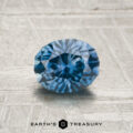 A 1.08-carat heated Montana sapphire in an oval cut is displayed on a textured gray surface, with the "Earth's Treasury" logo and text shown below.