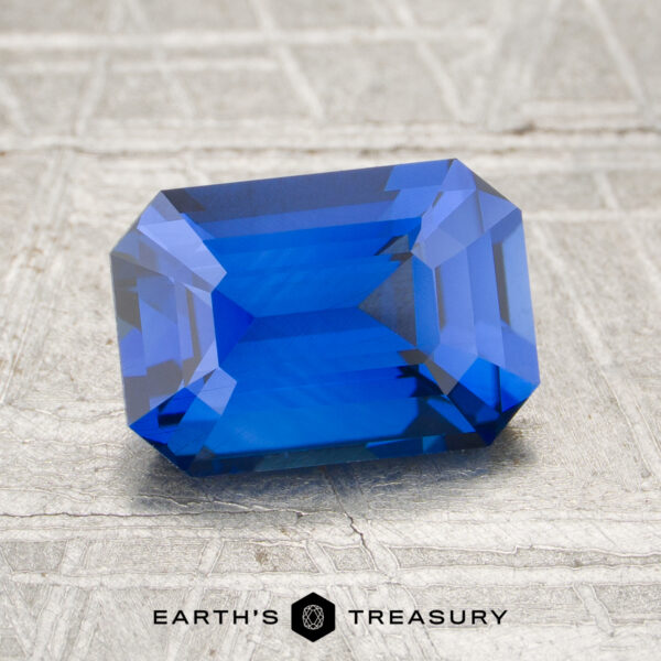 2.13-Carat Intense Blue Ceylon Sapphire (Heated) A 2.13-carat heated sapphire, rectangular and blue with step-cut facets, is displayed on a textured gray surface. "EARTH'S TREASURY" appears at the bottom of the image.