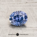 A 1.08-carat heated Montana sapphire with an oval cut is displayed on a textured light surface, featuring the text "EARTH'S TREASURY" and a geometric logo below.