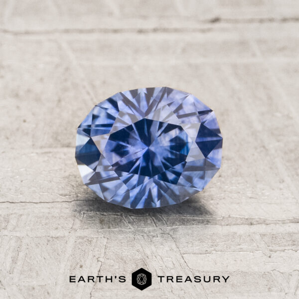 1.08-Carat Blue to Purple Color-Change Montana Sapphire (Heated) A 1.08-carat heated Montana sapphire with an oval cut is displayed on a textured light surface, featuring the text "EARTH'S TREASURY" and a geometric logo below.