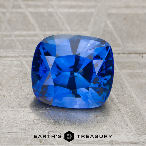 2.34-Carat Sapphire (Heated) A 2.34-carat heated sapphire with a cushion cut is displayed on a textured surface, with "Earth’s Treasury" written below.