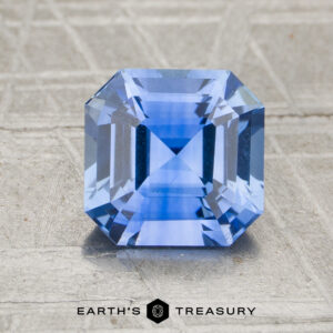 A 2.29-carat heated sapphire with a square step cut is shown on a textured surface, with "Earth's Treasury" written below it.