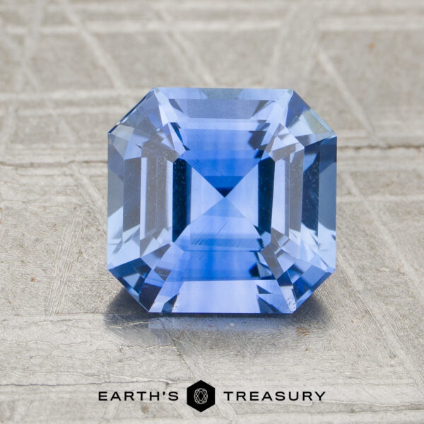 2.29-Carat Sapphire (Heated) A 2.29-carat heated sapphire with a square step cut is shown on a textured surface, with "Earth's Treasury" written below it.