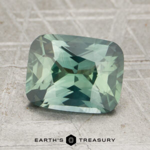 A 2.14-carat heated sapphire with a rectangular cushion cut is displayed on a textured grey surface, with "EARTH'S TREASURY" written at the bottom.
