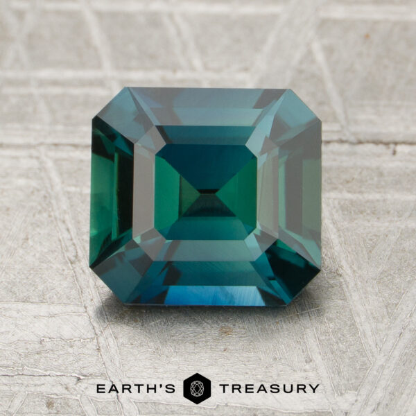 2.11-Carat Sapphire (Heated) A 2.11-carat heated sapphire with an emerald cut is shown on a textured gray surface, with "EARTH'S TREASURY" at the bottom.
