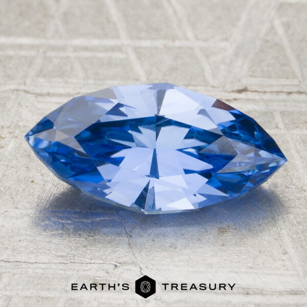 2.06-Carat Sapphire (Heated) A 2.06-carat heated sapphire, marquise-cut and blue, displayed on a textured surface with the "Earth's Treasury" logo below.