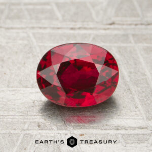 A 1.30-carat oval-cut ruby is displayed on a textured metallic surface, with the "Earth's Treasury" logo beneath it.