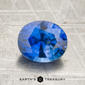Oval-cut 2.41-carat Ceylon Sapphire (Heated) displayed on a textured surface, with "EARTH'S TREASURY" and a logo shown beneath the gemstone.