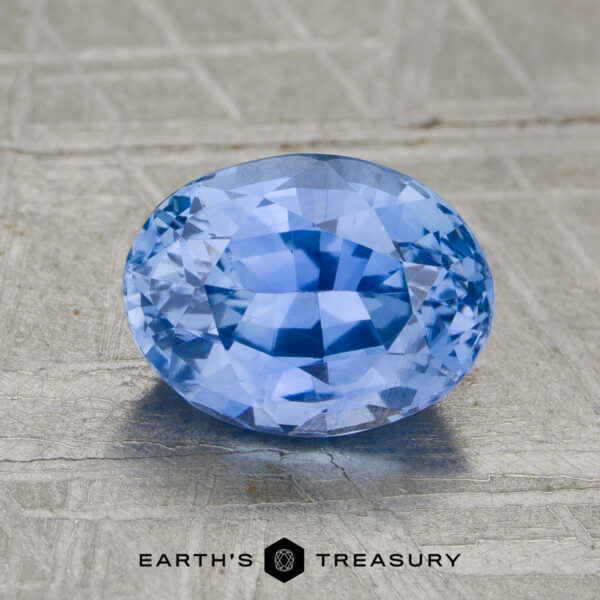 2.02-Carat Sapphire (Heated) 2.02-carat heated sapphire, oval-cut and blue, displayed on a textured gray surface with "EARTH'S TREASURY" text and logo beneath.