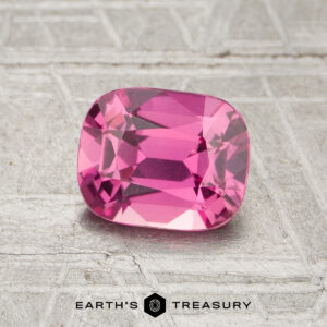 A 1.30-carat heated sapphire with a cushion cut is displayed on a textured metallic surface featuring the "Earth's Treasury" logo at the bottom.
