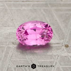Oval-cut pink 1.16-carat heated sapphire on a textured metallic surface, with "Earth's Treasury" and logo text at the bottom of the image.