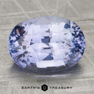 Unheated 4.12-carat oval-cut light violet sapphire with facets rests on a textured surface. "EARTH'S TREASURY" logo and text appear at the bottom of the image.