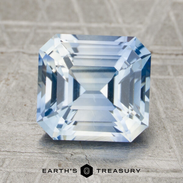 3.19-Carat Sky Blue Ceylon Sapphire (Heated) A 3.19-carat unheated sapphire with rectangular step-cut facets is shown on a textured surface, with the Earth's Treasury logo beneath it.