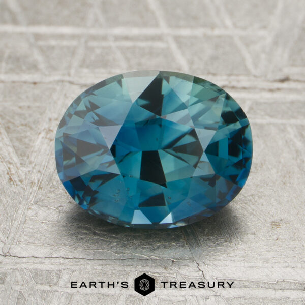 2.44-Carat Rich Teal Madagascar Sapphire (Unheated) A 2.44-carat unheated sapphire with an oval cut and blue-green hue rests on a light textured surface, with “EARTH'S TREASURY” displayed at the bottom.