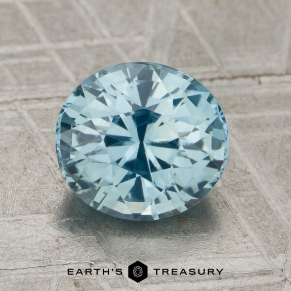 2.36-Carat Aqua Blue Madagascar Sapphire (Unheated) A 2.36-Carat Unheated Sapphire, faceted in an oval shape and light blue in color, rests on a textured surface with the "Earth's Treasury" name and hexagon logo visible below.