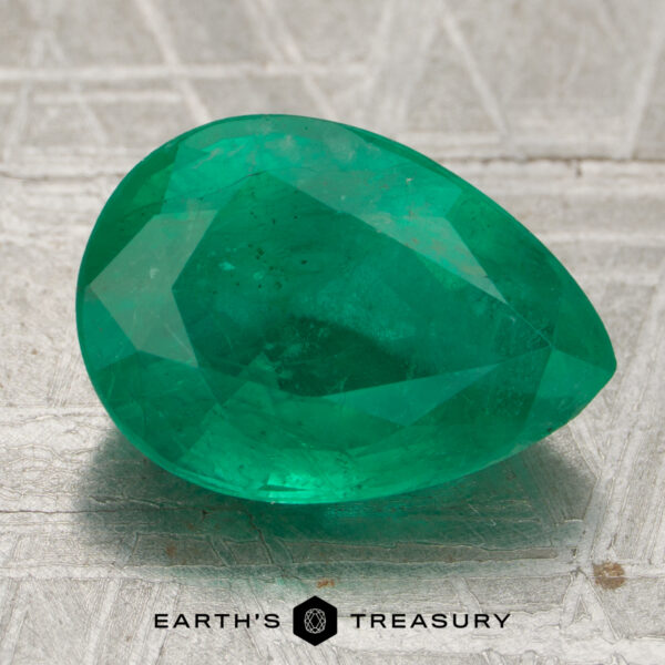 4.39-Carat Zambian Emerald (Oiled) A 4.39-carat emerald, pear-shaped and faceted, rests on a textured metallic surface. "EARTH'S TREASURY" appears at the bottom of the image.