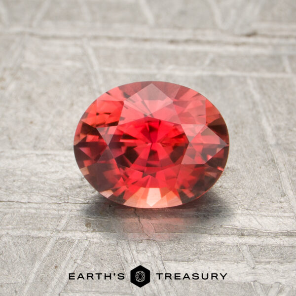 1.11-Carat Intense Orange Ceylon Sapphire (Heated) A 1.11-carat heated oval-cut sapphire with intricate facets rests on a textured gray surface, with "Earth's Treasury" displayed below.