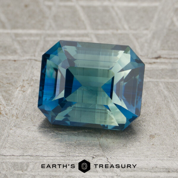 2.30-Carat Green-Blue Particolored Madagascar Sapphire (Unheated) A 2.30-carat unheated sapphire, emerald-cut in blue-green hues, is shown on a metallic textured surface with the Earth’s Treasury logo at the bottom.