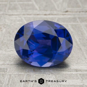 A 2.24-carat oval-cut blue gemstone is displayed on a textured surface with "EARTH'S TREASURY" written at the bottom.