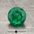 A 1.34-carat round-cut emerald gemstone displayed on a textured gray surface with "EARTH'S TREASURY" at the bottom.