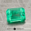A 2.29-carat Colombian emerald with visible inclusions rests on a textured metallic surface, with the "Earth's Treasury" logo and text displayed at the bottom.