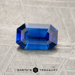 A 0.95-carat Ceylon Sapphire (Heated), rectangular and deep blue, rests on a textured gray surface with "Earth's Treasury" below.