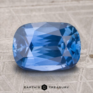 A 3.96-carat heated Ceylon sapphire gemstone with a cushion cut is displayed on a textured surface, featuring the "Earth's Treasury" logo at the bottom.