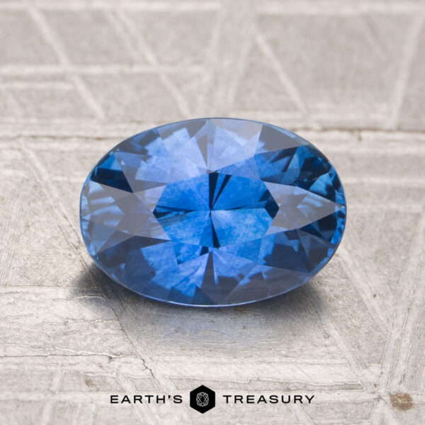 2.05-Carat Ceylon Sapphire (Heated) A 2.05-carat heated Ceylon sapphire, cut in a faceted oval shape, rests on a textured metallic surface with "EARTH'S TREASURY" branding at the bottom.
