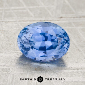 2.02-carat heated sapphire, oval-cut and blue, displayed on a textured gray surface with "EARTH'S TREASURY" text and logo beneath.