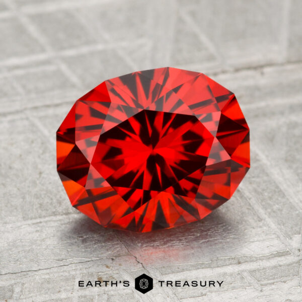 3.01-Carat Spessartine Garnet A 3.01-carat spessartine garnet, faceted in an oval cut, is displayed on a textured gray surface with "Earth's Treasury" at the bottom.