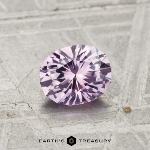 0.96-Carat Lilac Pink Montana Sapphire A 0.96-carat Montana sapphire, faceted in an oval cut and displaying pale purple hues, rests on a textured grey surface with the Earth's Treasury logo below.